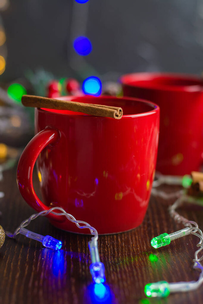 赤のカップにシナモンとおいしいマルチワインアルコール暖かい飲み物。新年の休日を待っているの概念。クリスマス・ガーランドとボケを背景に. - 写真・画像
