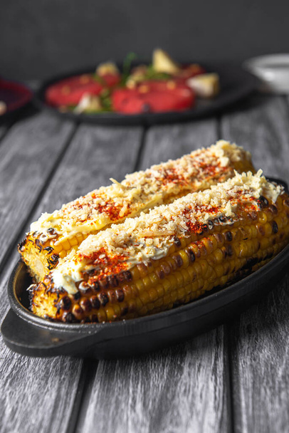 Delicious golden grilled corn on the cob served indoors with spices and cheese on top. Served in a tray over rustic grey wooden table background. Dinner idea. - Valokuva, kuva