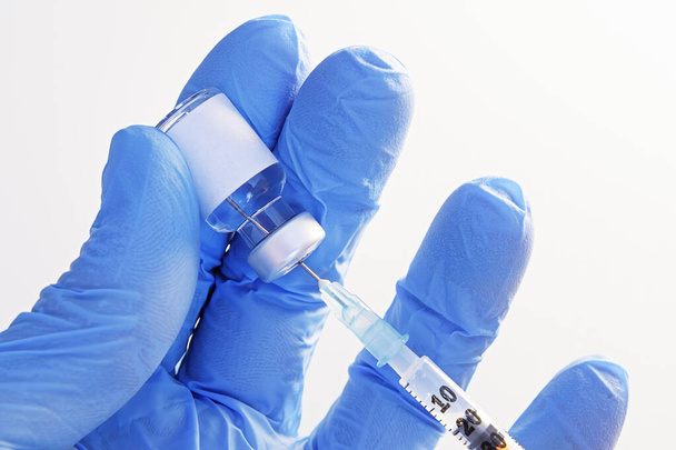 Close-up van de hand in handschoenen die een ongemarkeerde injectieflacon vasthouden en vloeistof uit de spuit halen voor injectie. Begrippen gezondheidszorg, geneeskunde, farmacie en vaccinatie - Foto, afbeelding