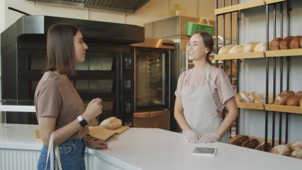 Slowmo відстежити знімок щасливої молодої жінки-контрабандистки в фартухах і рукавичках розмовляючи з жіночим клієнтом в затишній пекарні
 - Кадри, відео