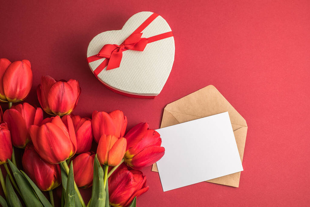 Csokor vörös tulipán és ajándék szív doboz elszigetelt piros háttérrel. Tavaszi virágok. Anyák napja, Születésnap, Nő napja, Esküvő, Valentin nap. Lapos fekvés. Másold a helyet. Zászlós - Fotó, kép