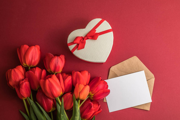 Kimppu punainen tulppaanit ja lahja sydän laatikko eristetty punaisella pohjalla. Kevätkukkia. Äitienpäivä, Häät, Syntymäpäivä, Ystävänpäivä, Nainen. Litteä pano. Kopioi tilaa. Banneri - Valokuva, kuva