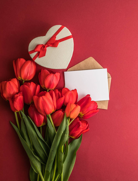 Boeket rode tulpen en geschenkdoos geïsoleerd op rode achtergrond. Voorjaarsbloemen. Wenskaart voor Verjaardag, Vrouw, Moederdag, Bruiloft, Valentijnsdag. Plat gelegd. Begrepen, ruimte. Banner - Foto, afbeelding