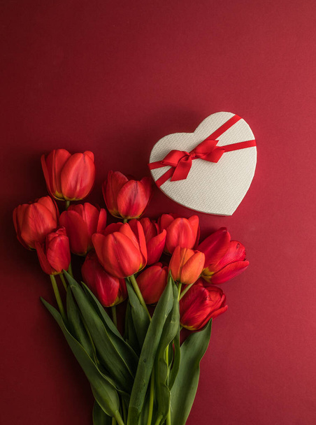 Bouquet of red  tulips and gift heart box isolated on red background . Spring flowers. Greeting card for Birthday, Woman, Mother's Day, Wedding, Valentines day. Flat lay. Copy space. Banner - Photo, Image