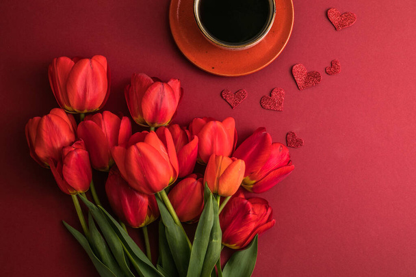 poranna kawa i bukiet czerwonych tulipanów na jasnoczerwonym tle. Widok z góry.Kopiuj miejsce na tekst. Pojęcie wakacji. - Zdjęcie, obraz