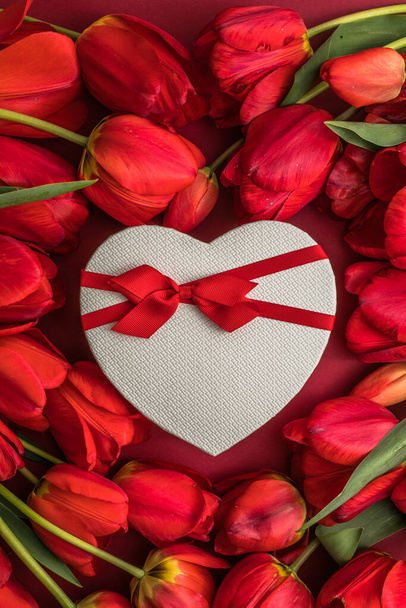 Bukiet czerwonych tulipanów i pudełko z prezentem dla serca, aranżacja z dużą ilością miejsca na tekst. Wiosenny nastrój. Kartka z pozdrowieniami na urodziny, Kobieta, Ślub, Walentynki. - Zdjęcie, obraz