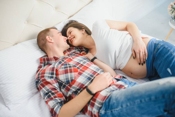 Happy pregnant family lies on the house bed. - Photo, image