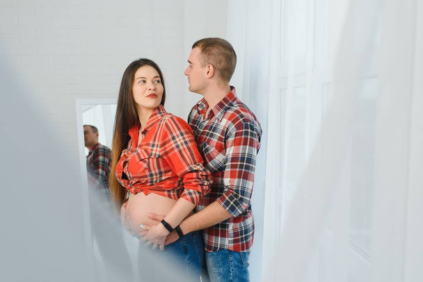 Loving man hugging his pregnant wife from behind standing near window at home, copy space - Fotoğraf, Görsel