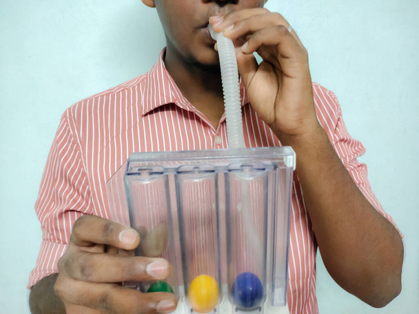 Person blowing Triball incentive Spirometer useful for the purpose of Respiratory Exercise mainly for the Breathing problem people or Elderly people to get the normal breathing level isolated in a yellow background - Foto, imagen