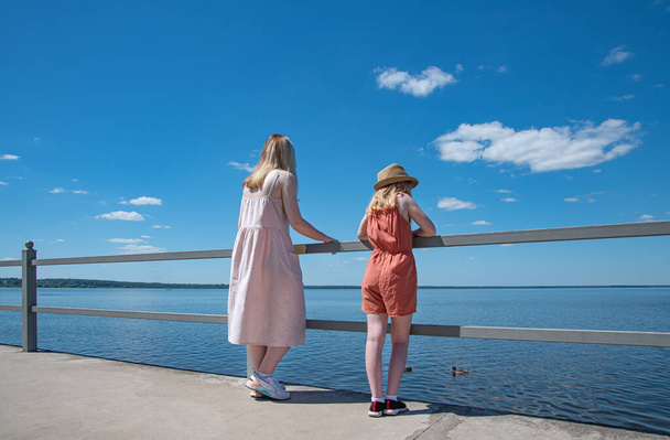 Two girls  stands on the seafront  and looks dreamily into the distance on a sunny summer day, panorama view. Without face - Foto, immagini