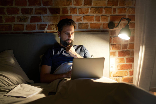 Hombre acostado en la cama y el uso de ordenador portátil                                - Foto, Imagen