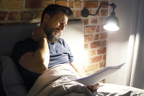 Exhausted man with documents working late in bed                                - 写真・画像