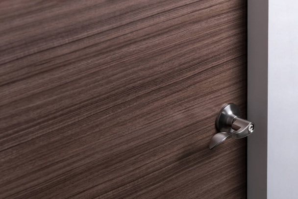 detail of wooden door with stainless steel handle with keyhole, wave style lever handle door knob with lock, modern interior design concept, image with copy space, shallow depth of field - Photo, Image
