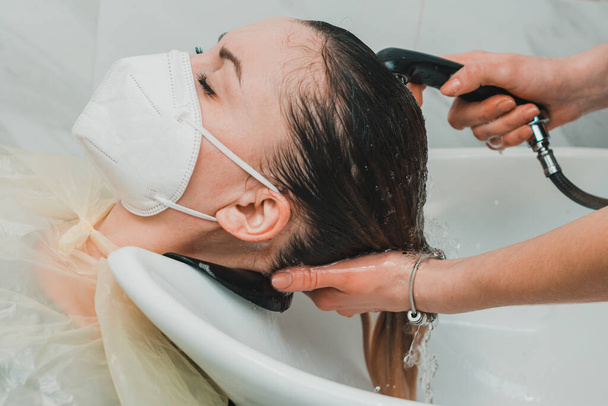 Dünya karantinası sırasında kuaför, bir güzellik salonunda başını yıkamak, maskeli bir müşteri. yeni - Fotoğraf, Görsel