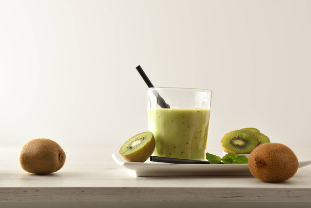 Kiwi drink glass presentation on plate with cut fruit on wooden table with isolated background. Front view. - Foto, Bild
