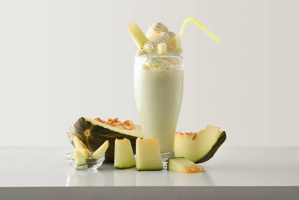 Melon milkshake with cream decorated with fruit around on white table and light isolated background. Front view. - Φωτογραφία, εικόνα