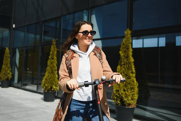 Young beautiful woman riding an electric scooter to work, modern girl, new generation, electric transport, ecology, ecological transport, sunset, electric skateboard. - Foto, Imagen