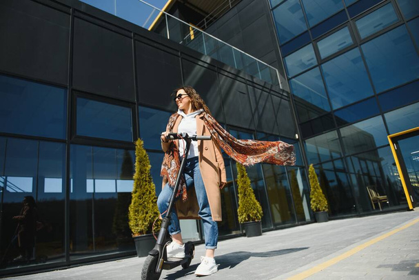 Young beautiful woman riding an electric scooter to work, modern girl, new generation, electric transport, ecology, ecological transport, sunset, electric skateboard. - 写真・画像