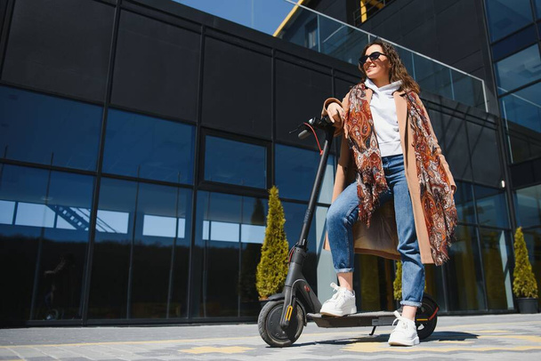 Young beautiful woman riding an electric scooter to work, modern girl, new generation, electric transport, ecology, ecological transport, sunset, electric skateboard. - Foto, afbeelding