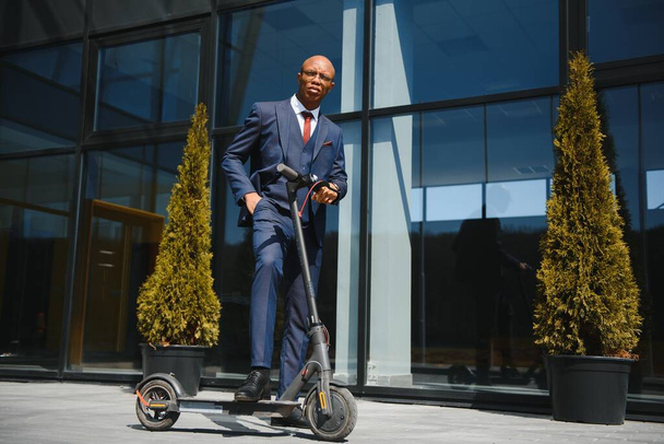 businessman with electric scooter standing in front of modern business building talking on phone. - Foto, Bild