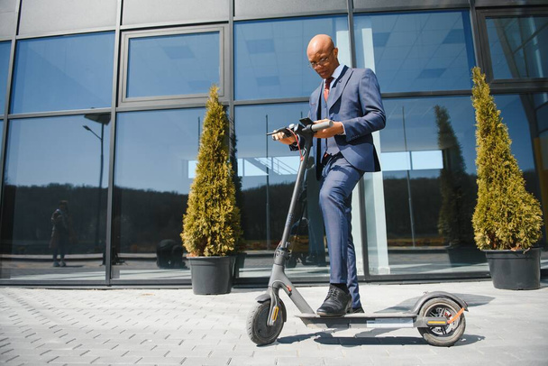 businessman with electric scooter standing in front of modern business building talking on phone. - Foto, Bild
