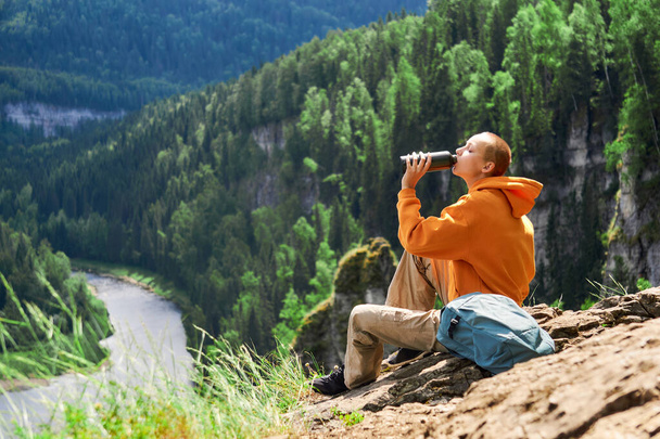 tienermeisje wandelaar rusten en drinken op de rand van een klif kijken naar de rivier tegen de achtergrond van een natuurlijk landschap - Foto, afbeelding