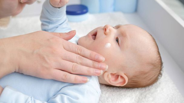 Close-up da mãe aplicando creme hidratante do bebê para evitar a pele seca. Conceito de higiene, cuidado do bebê e cuidados de saúde - Foto, Imagem