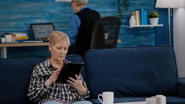 Orta yaşlı bir kadın, elinde tablet, e-kitap okuyor. - Fotoğraf, Görsel
