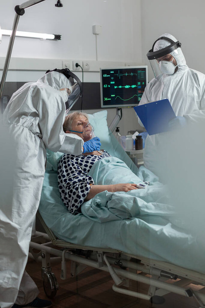 Personal médico en traje ppe que ayuda al paciente a respirar con máscara de oxígeno - Foto, Imagen