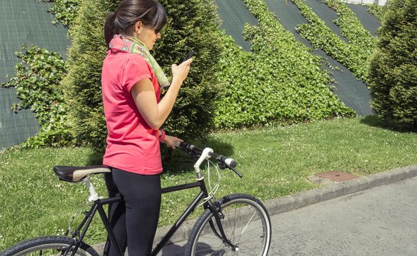 Donna sportiva con fixie bike alla ricerca di smartphone
 - Foto, immagini