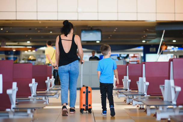 Family at airport before flight. Mother and son waiting to board at departure gate of modern international terminal. Traveling and flying with children. Mom with kid boarding airplane. yellow family - Fotoğraf, Görsel