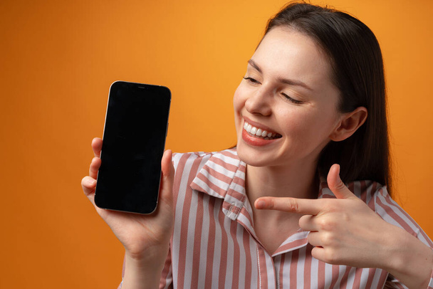 Happy smiling young woman showing you black smartphone screen with copy space - Photo, Image