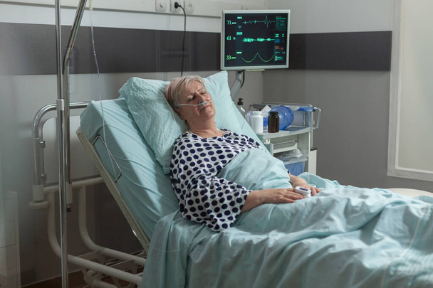 Mujer mayor descansando en la cama del hospital respirando con la ayuda de la máscara de oxígeno - Foto, Imagen