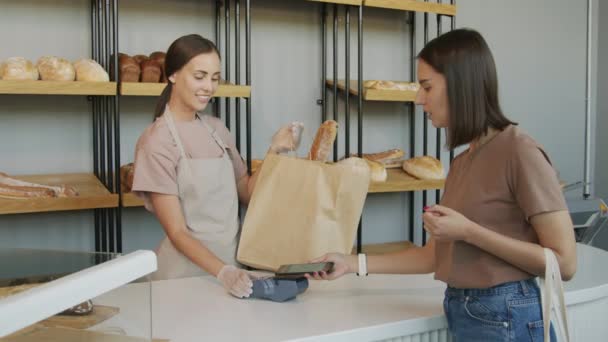 Slowmo záběr mladé ženy pomocí mobilního telefonu platit za čerstvě upečené zboží v útulné pekárně - Záběry, video