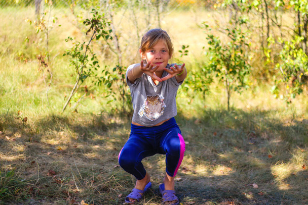 Defocus kaukasischen preteen Mädchen, die körperliche Bewegung im Park, Wald, im Freien, draußen. Gesunder Wellness-Lebensstil. Kniebeugen mit ausgestreckten Armen. Natur Sommer grünen Hintergrund. Unscharf - Foto, Bild