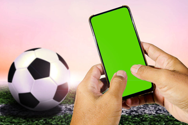 green blank screen mobile phone in man's hand with football background - Photo, Image