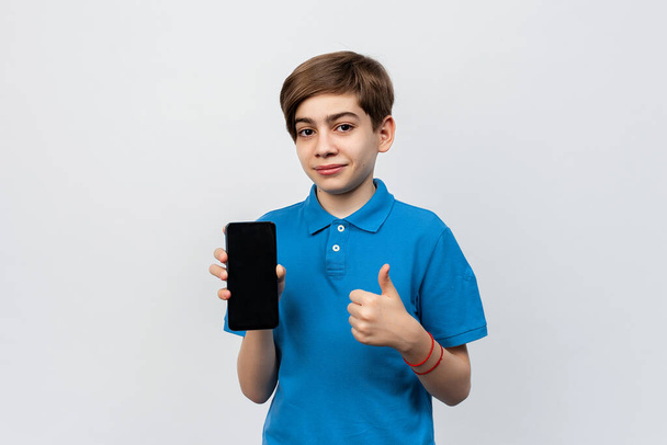 Portrait of pretty boy pointing finger at smartphone screen, showing app, recommending mobile application or online shopping store, standing against light gray background - Foto, Bild