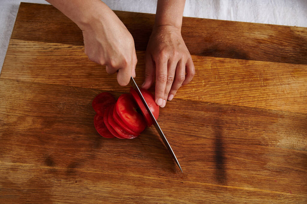 Top view of woman hand cutting tomato on a wooden board - Photo, image