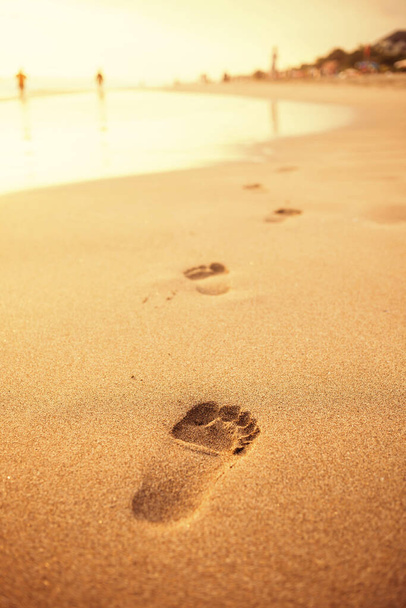 Human's footprints on a yellow sand at golden hour on a seaside. Symbol of a lonely life. - Foto, immagini