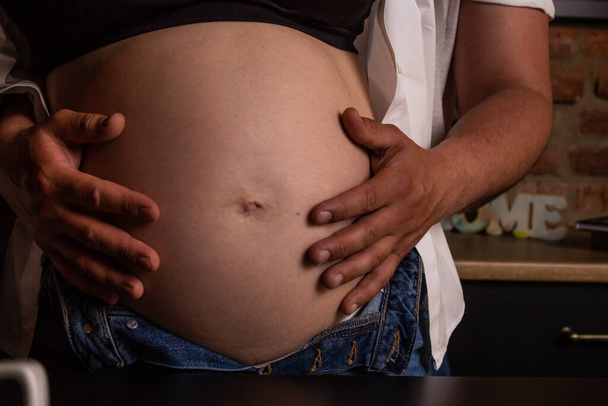Közelkép egy terhes hasáról egy leendő apa kezében lévő lányról. - Fotó, kép