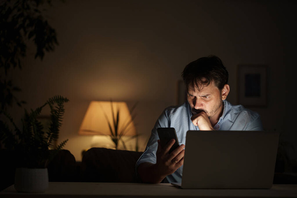 young male businessman works at home at night on laptop, working from home office, studying online, . Internet addiction or man working late at night. thoughtful man works late at night in home office - Photo, image
