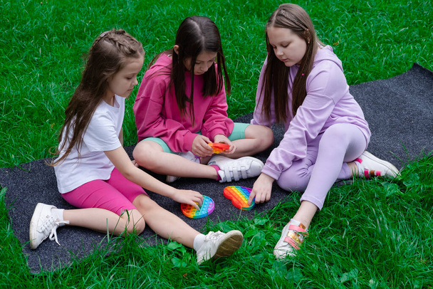 kolme teini tytöt värikkäissä vaatteissa pelata trendikäs aistillinen lelu pop se outdors. sateenkaaren pehmeät silikonikuplat. ahdistuneisuus relif, antistress, mielenterveyden käsite. Anti stressi peli popit.  - Valokuva, kuva