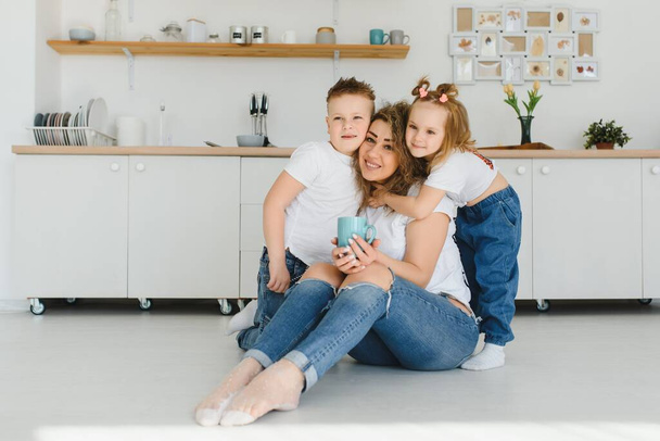 Happy young family, mom with little children sit on warm wooden floor in new modern design kitchen, mother with excited small kids relax rest in own renovated apartment, moving concept - Zdjęcie, obraz