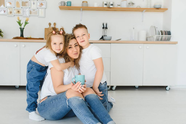 Happy young family, mom with little children sit on warm wooden floor in new modern design kitchen, mother with excited small kids relax rest in own renovated apartment, moving concept - Foto, immagini