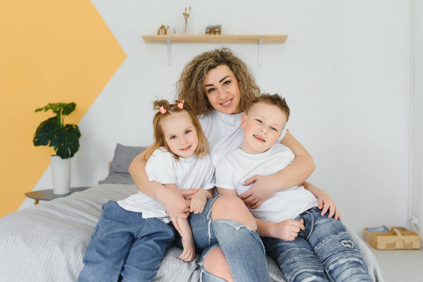 Portrait of smiling young mommy embracing kids little son and daughter. Happy family. Mother with children sitting on bed and loving the good times together. Closeup - Фото, зображення