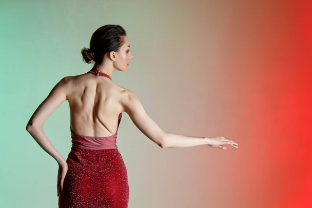 Colored background, neon lights, studio shot. Portrait of a young elegant brunette woman in a beautiful dress. Naked back, interesting poses - Foto, afbeelding