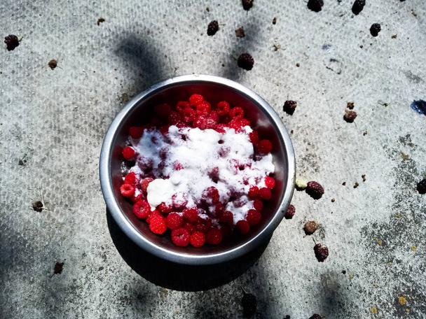 Frambuesas rojas en un tazón de metal lleno de agua, en un tazón sin agua, en un tazón espolvoreado con azúcar en un tazón lleno de crema - Foto, imagen