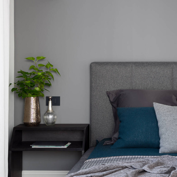 Close-up on simple, black nightstand with decorations next to comfortable bed with stylish bedclothes - Foto, Bild