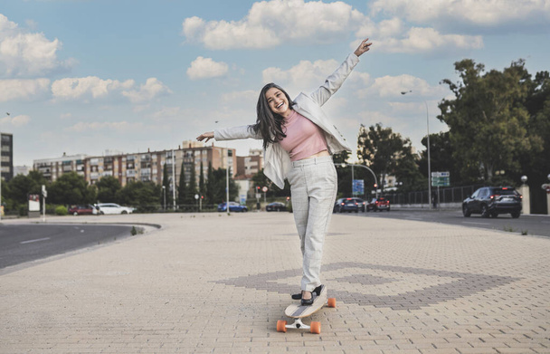 довольно зрелая женщина развлекается со скейтбордом, носит деловую одежду - Фото, изображение