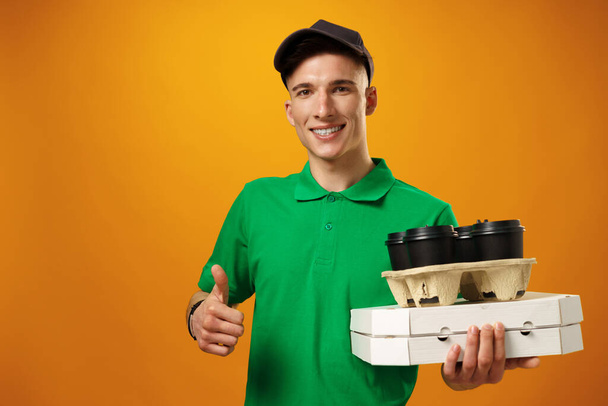 Happy young delivery man holding pizza box against yellow background - Foto, immagini